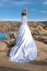 Novia con vestido blanco largo de espaldas levantando el ramo frente a rocas y un lago en Arizona